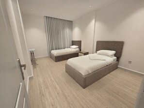 Ett modernt hotellrum med två sängar, ett sängbord, en lampa och ett stort fönster med gardiner.