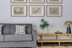 A living room with a grey sofa, a wooden side table, and a plant. - Vatican City View 2BR & 2BA Home and More (Roma)
