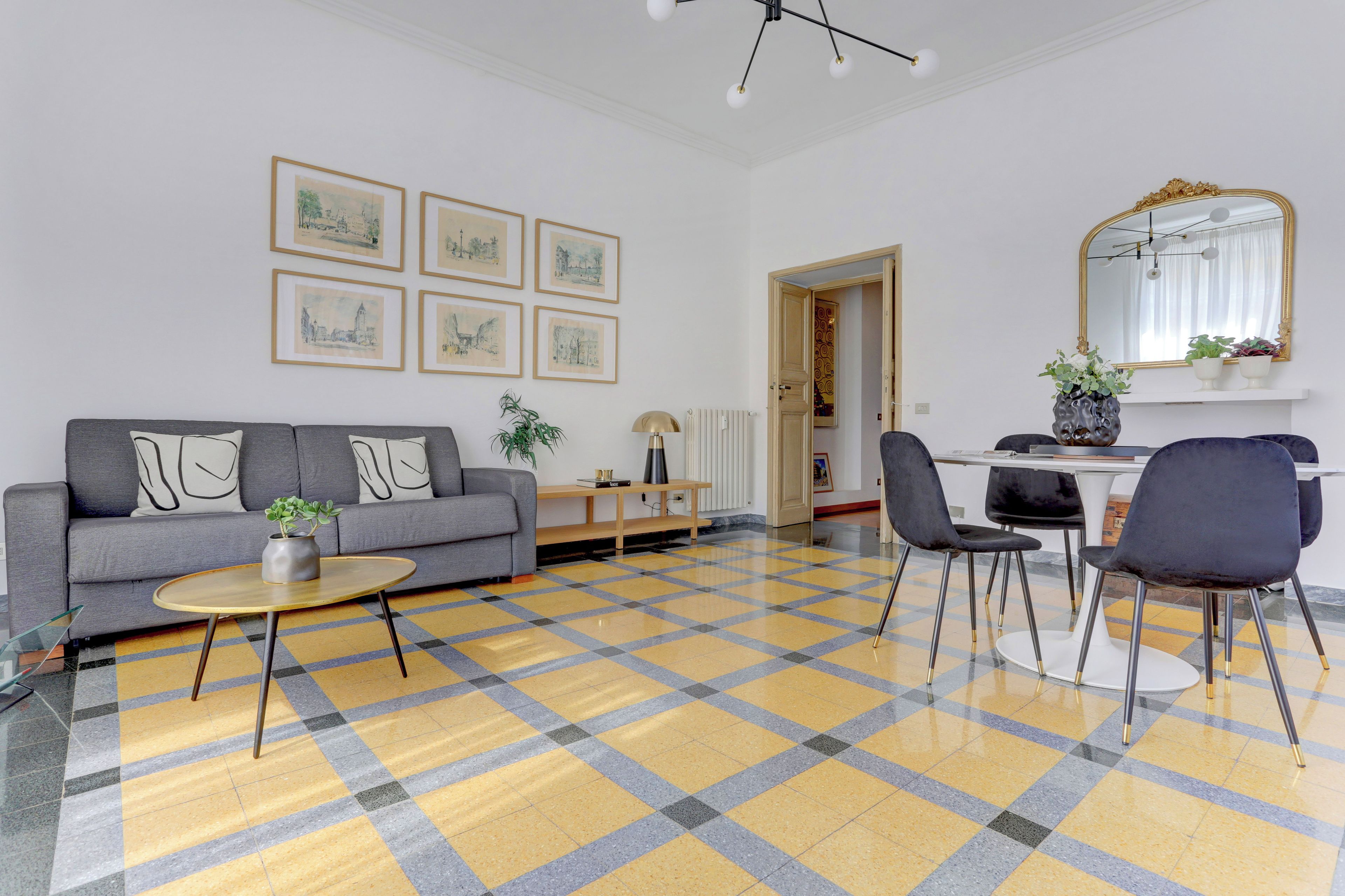 Un salon comprenant un canapé, une table basse et des fauteuils, un coin repas avec une table et des chaises, et un couloir agrémenté d’un miroir et de tableaux encadrés au mur.