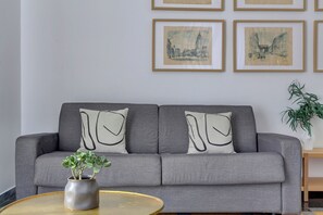Ein graues Sofa mit zwei Kissen, eine kleine Pflanze in einem grauen Topf und ein runder Couchtisch.