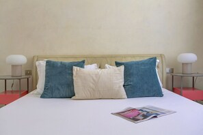 A bed with a white mattress, two blue pillows, a beige pillow, and a magazine on the bed. - Vatican City View 2BR & 2BA Home and More (Roma)