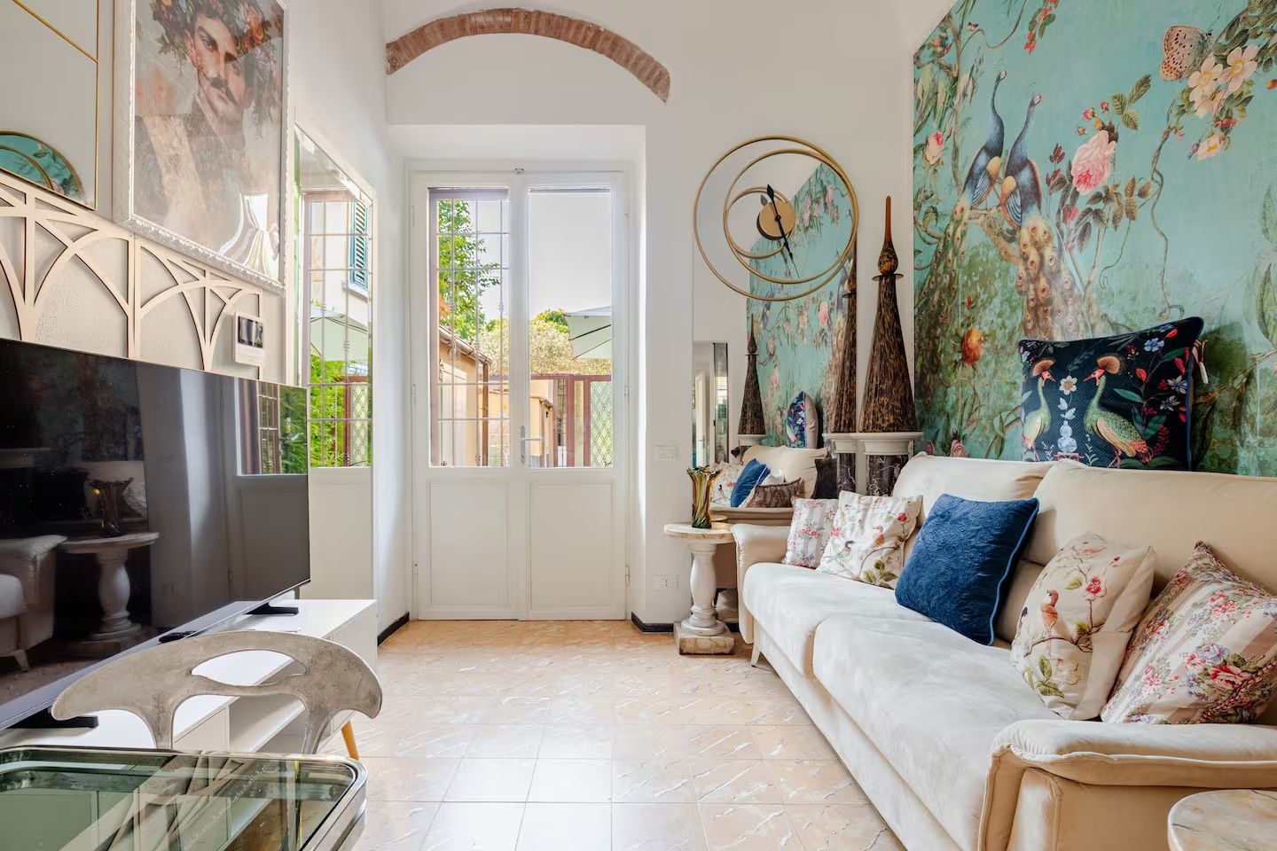Una sala de estar con televisor, un sofá con cojines estampados, un muro decorativo y una puerta que da al exterior.