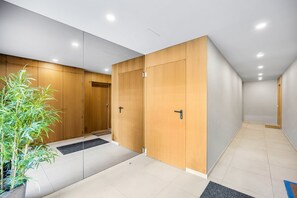 Moderni hotellikäytävä, jossa on puiset ovet, ruukkuistutettu kasvi ja laatoitettu lattia.