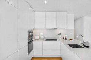 A modern kitchen with white cabinetry, a built-in oven, a toaster, a kettle, and a sink with a faucet. - Douro Atlântico II | Terrace & Sea Views (Canidelo)