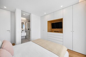 A bedroom with a bed, a built-in TV, a wardrobe, and a bathroom with a shower and mirror. - Douro Atlântico II | Terrace & Sea Views (Canidelo)