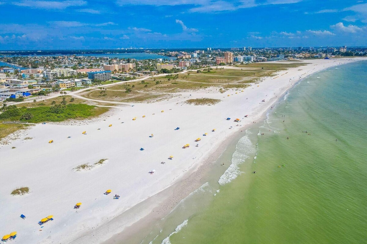 A coastal cityscape with a wide sandy beach, a marina, and a dense urban area with high-rise buildings.