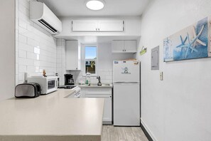 A modern kitchen with white cabinetry, a built-in microwave, a toaster, a coffee maker, and a refrigerator with a Florida magnet. - Tropic Terrace (Treasure Island)