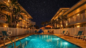 A swimming pool with a night sky view, surrounded by palm trees and lounge chairs. - Tropic Terrace (Treasure Island)