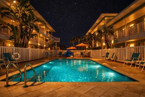 Piscina con vista al cielo nocturno, rodeada de palmeras y sillones de descanso.