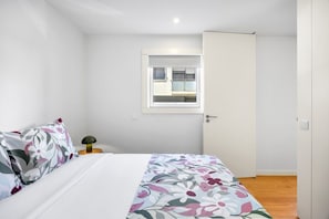 Ein Schlafzimmer mit einem Bett, einem Nachttisch, einer Lampe, einem Fenster und einer Tür.