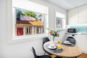 Eine moderne Küche mit Essbereich, Blick auf ein Gebäude mit roten Türen und eine Vase mit Blumen auf dem Tisch.