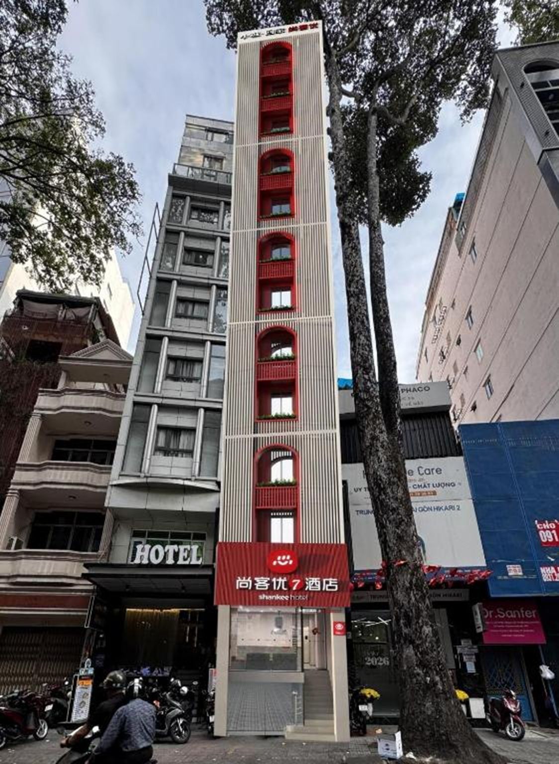 Un hotel con fachada vertical, varios balcones y un llamativo letrero rojo con el nombre del hotel.
