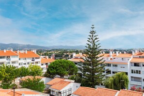 A residential area with white buildings and orange-tiled roofs, surrounded by greenery and mountains in the distance. - Duplex with Private Terrace and A/C in Cascais (Cascais)