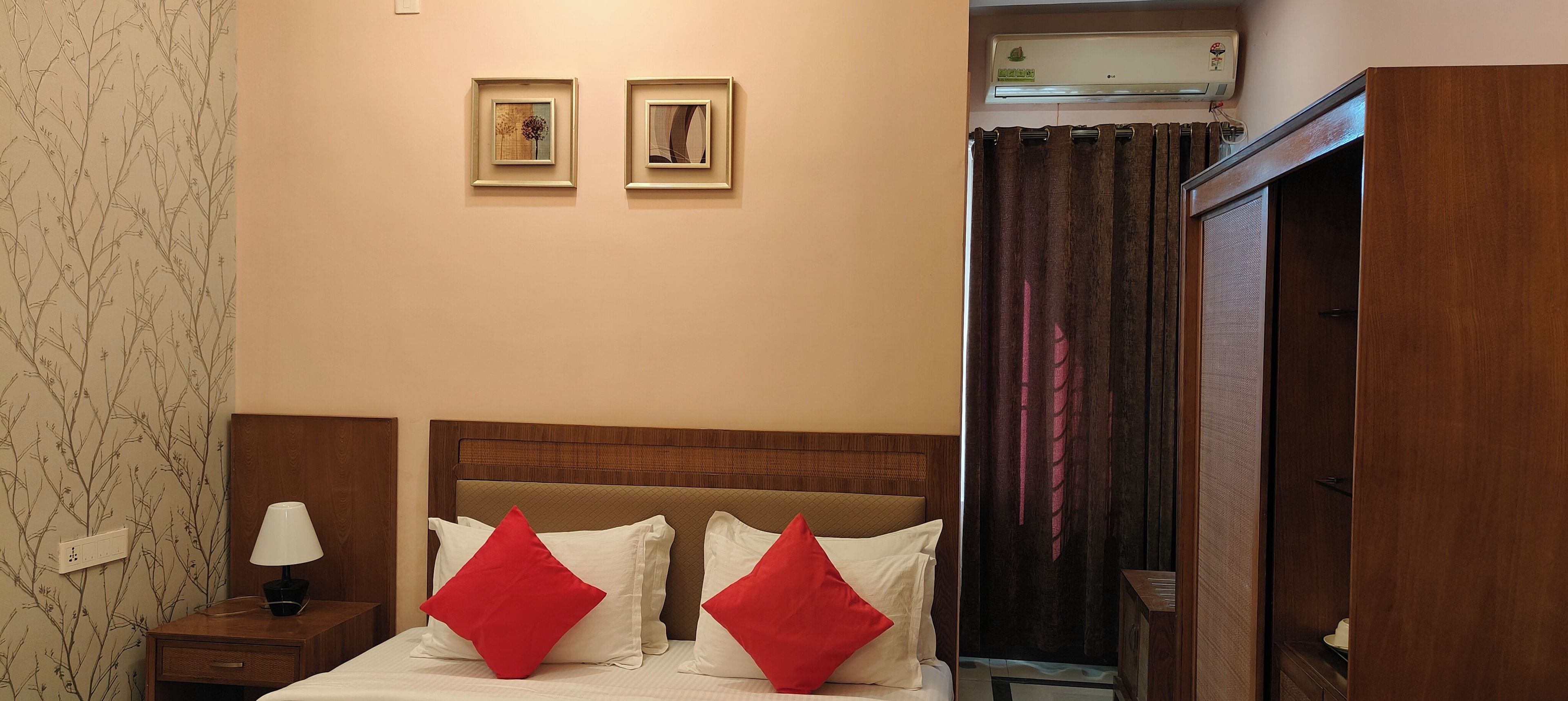 A hotel room with a bed, nightstand, lamp, two framed pictures on the wall, and an air conditioning unit.