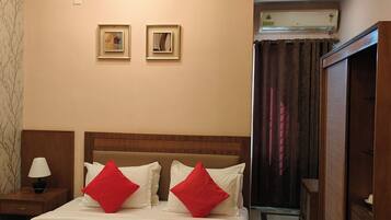 A hotel room with a bed, nightstand, lamp, two framed pictures on the wall, and an air conditioning unit.