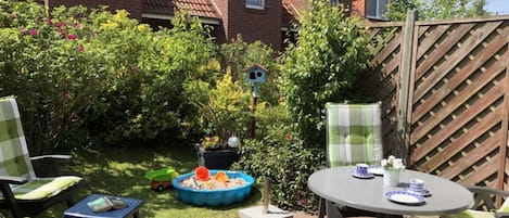 A patio area with a round table and chairs, a small play area with toys, and a birdhouse.