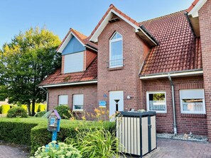 Ein zweistöckiges Backsteinhaus mit rotem Ziegeldach, einem sichtbaren Briefkasten und einem kleinen Garten mit verschiedenen Pflanzen.
