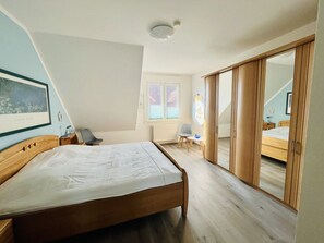 Ein Schlafzimmer mit Bett, Stuhl, Schreibtisch, Heizkörper, Fenster und einer Schiebetür.