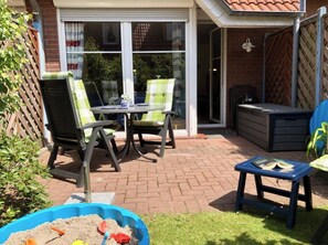 Eine Terrasse mit Tisch und Stühlen, ein kleiner, blauer Spielbereich und ein überdachter Sitzbereich.