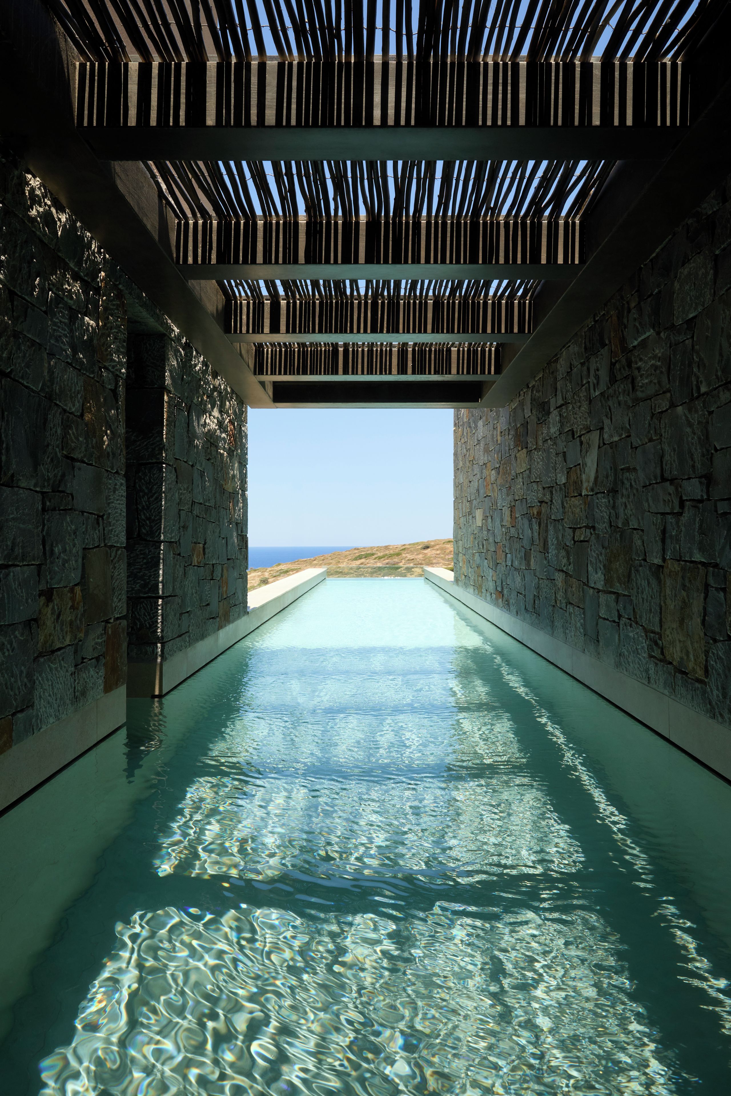 Una piscina infinita con vista despejada al océano, rodeada de muros de piedra y una estructura de techo de madera.