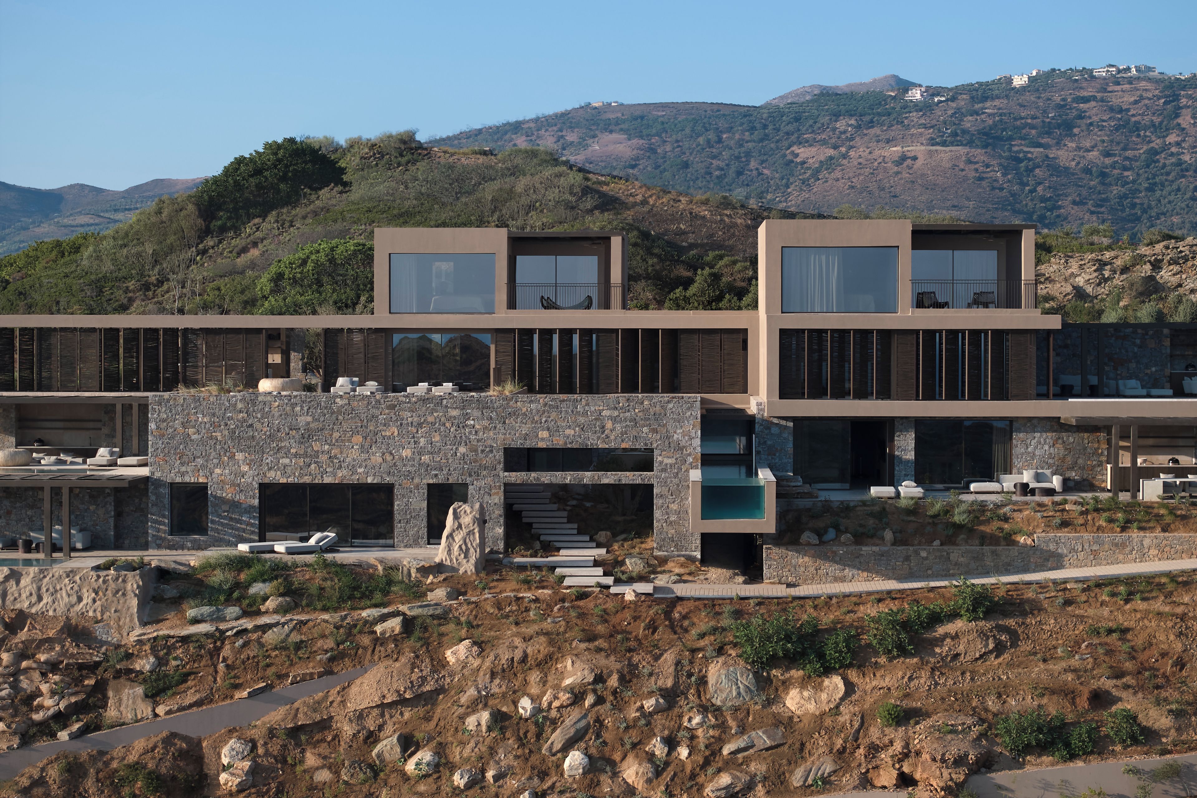Un edificio moderno de varios pisos con fachada de piedra, amplias ventanas y zonas de estar al aire libre.