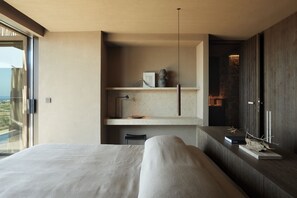 A modern bedroom with a large bed, a built-in shelf with decorative items, and a view of the outdoors.