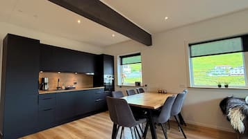 A modern kitchen with dark cabinetry, a wooden countertop, and a dining area with a wooden table and chairs.