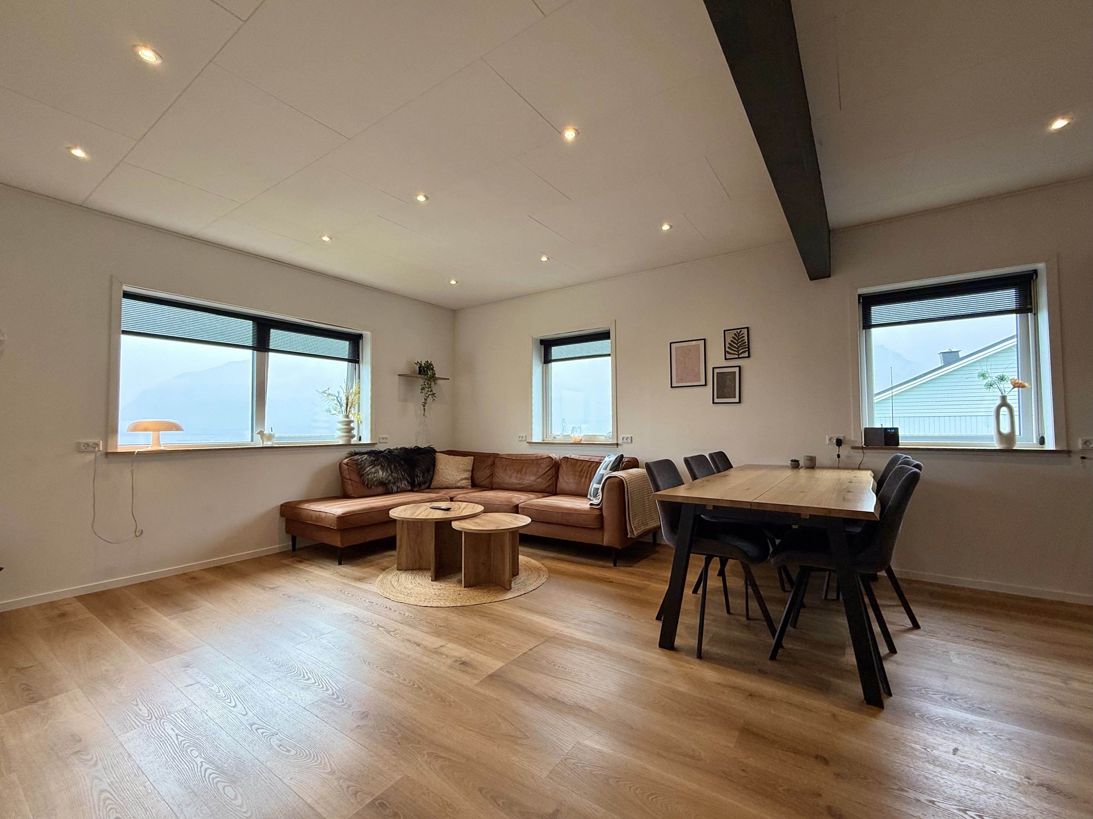 Un vaste espace de vie doté d’un plancher en bois, d’un canapé en cuir marron, d’une table basse ronde et d’une table à manger avec des chaises.