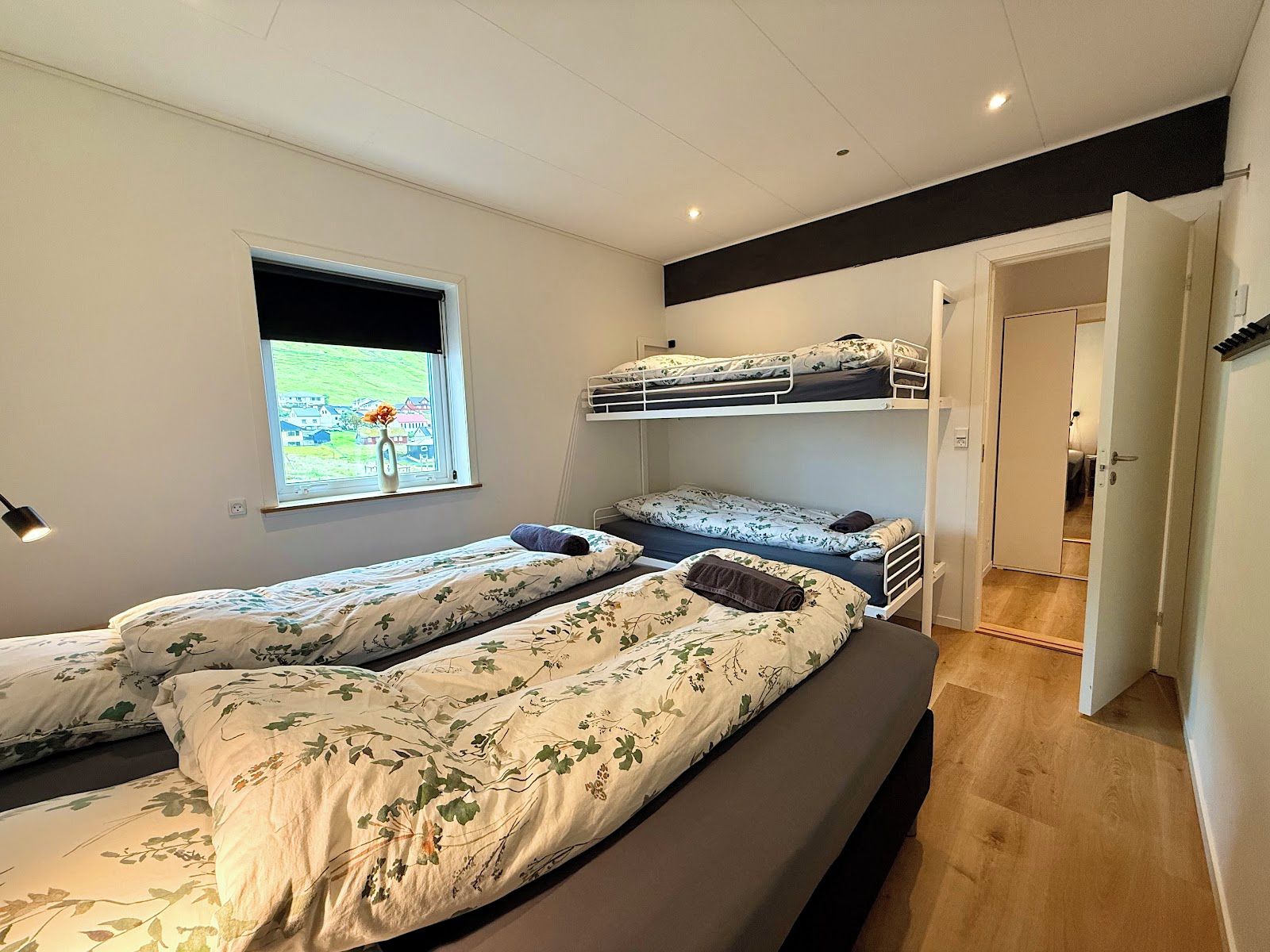 A room with bunk beds, a window with a view, and a door leading to another room.