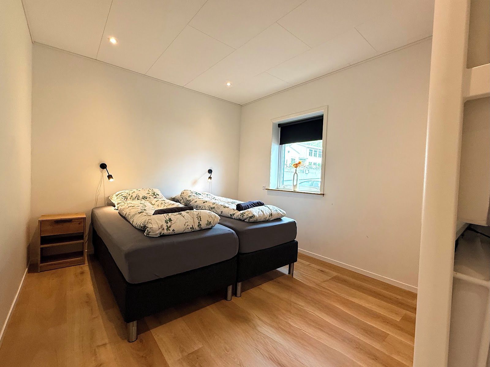Un dormitorio con cama, mesitas de noche, ventana y vistas al exterior.