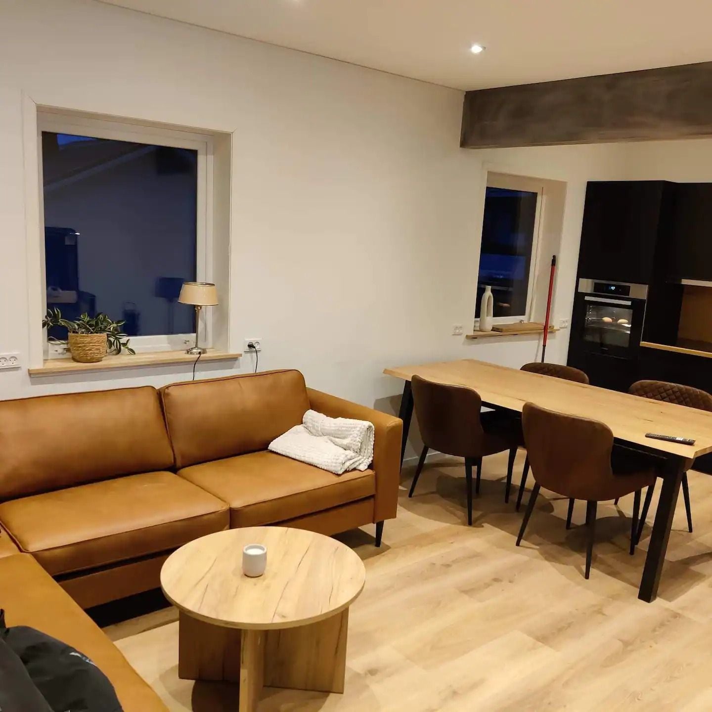 A modern living room with a brown leather sofa, a round wooden coffee table, and a dining area with a wooden table and chairs.