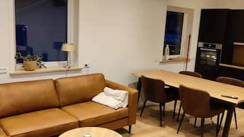 A modern living room with a brown leather sofa, a round wooden coffee table, and a dining area with a wooden table and chairs.