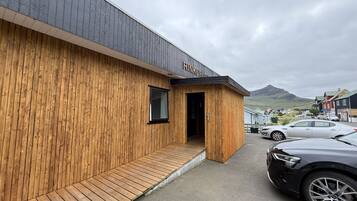 A wooden building with a nameplate, a small entrance, and a parking area with cars.