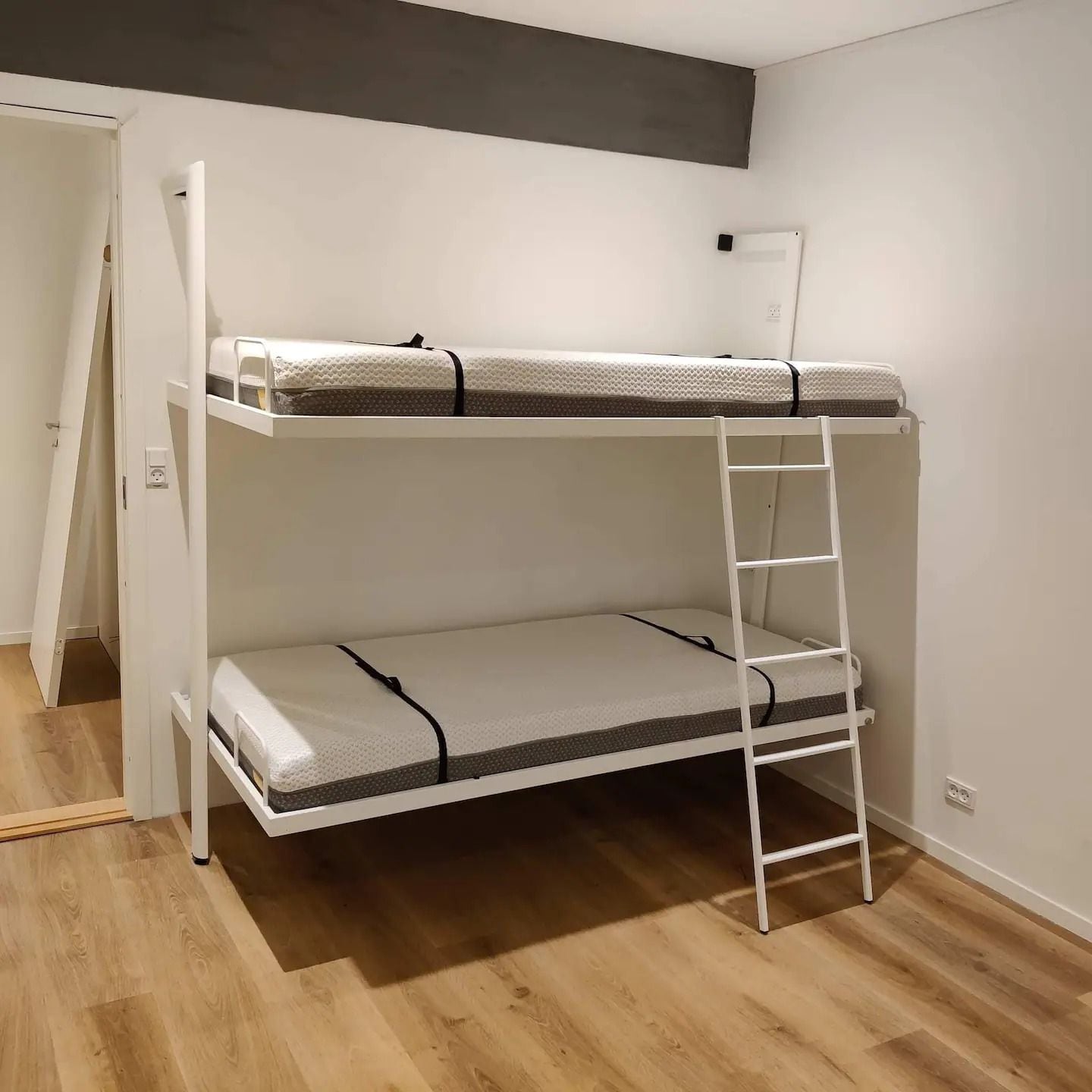 Una cama litera con escalera, pared blanca y suelo de madera.
