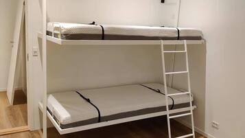 Una cama litera con escalera, pared blanca y suelo de madera.