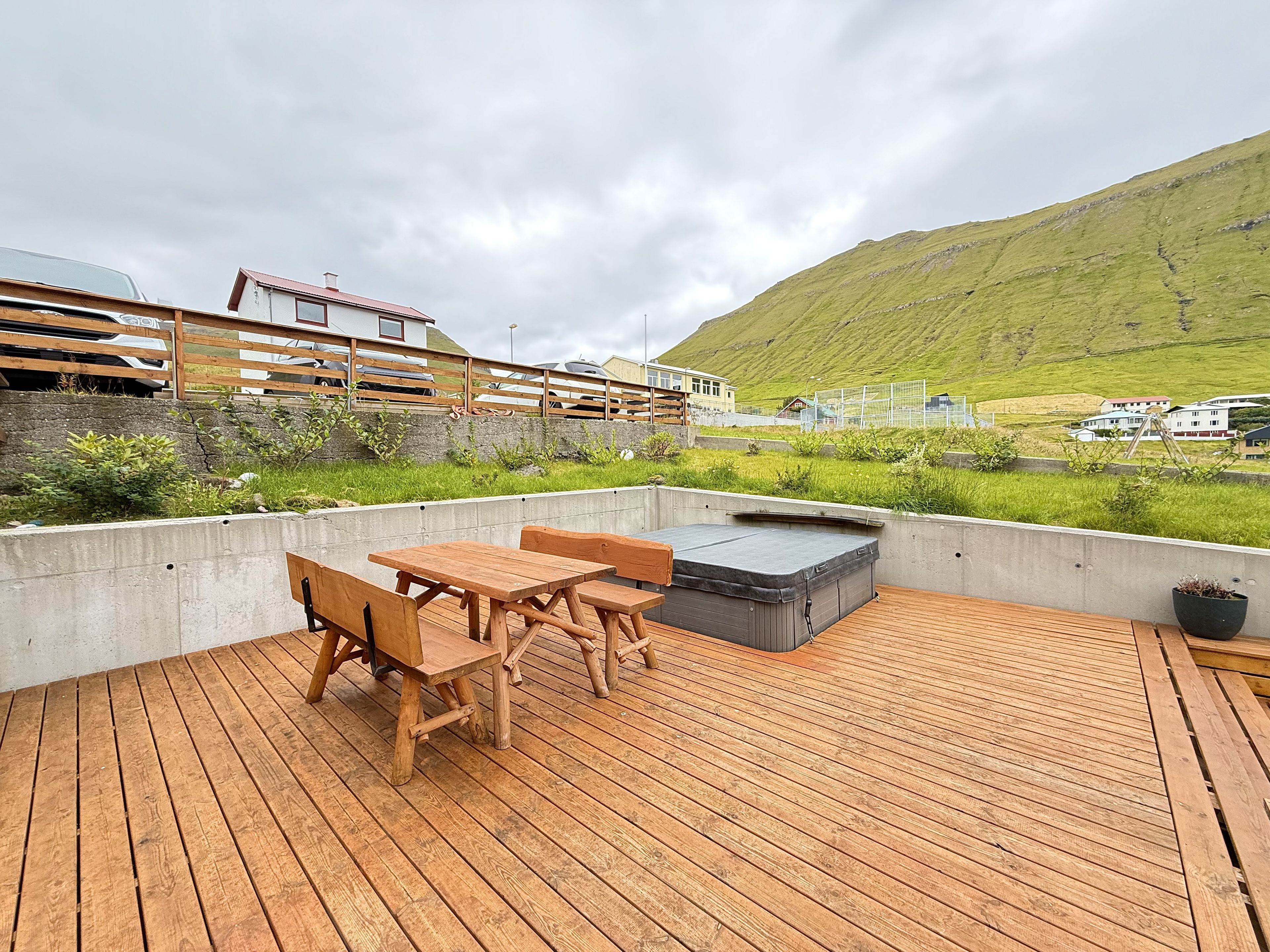 Una terraza de madera exterior con un jacuzzi y zona de estar, con vistas a una ladera verde.