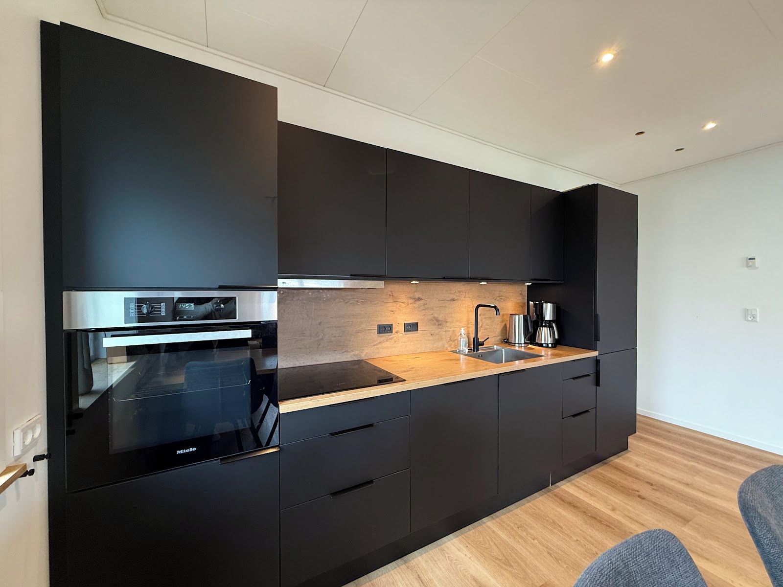 Une cuisine moderne avec des meubles de couleur noire, un four en acier inoxydable et un plan de travail en bois.