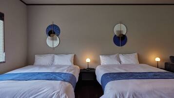 A hotel room with two beds, each with white bedding and a blue accent. There are wall-mounted light fixtures on either side of the beds.
