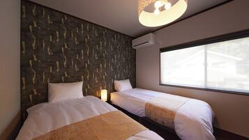 A hotel room with two beds, a patterned headboard, an air conditioning unit, and a window with blinds.