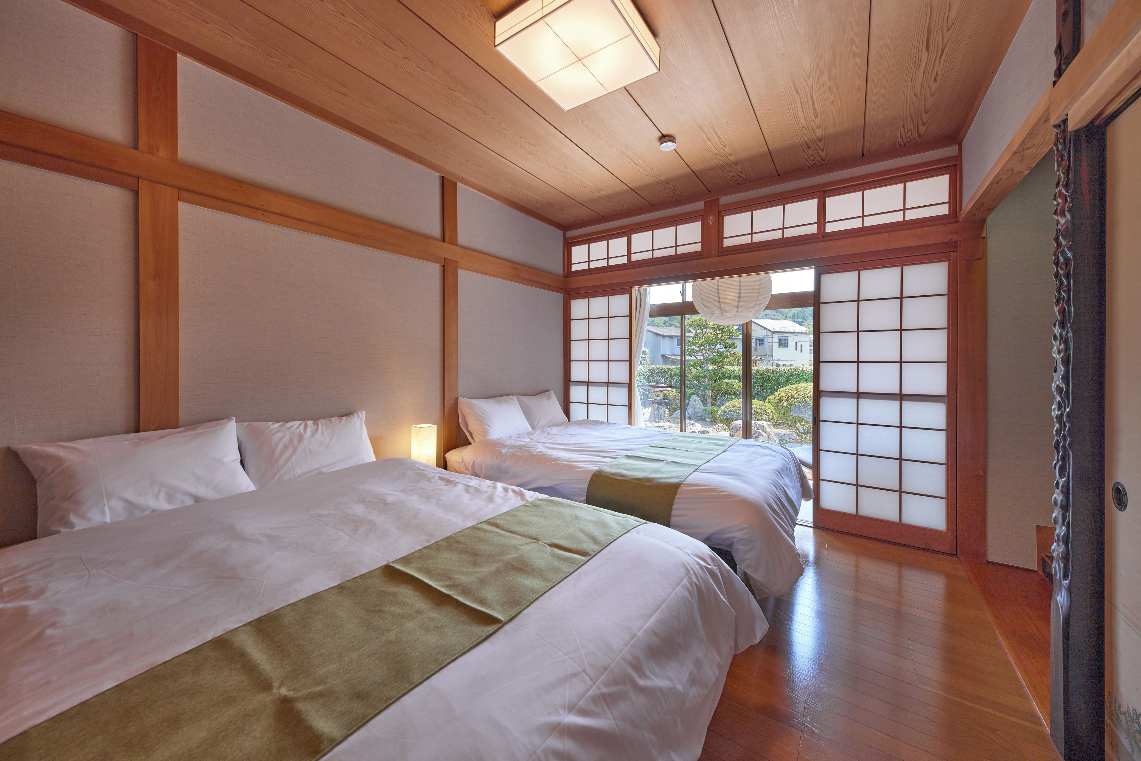 A traditional Japanese-style room with tatami flooring, two beds with white bedding, and a view of a garden through shoji screens.