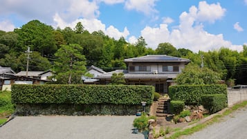 A traditional Japanese house with a tiled roof, surrounded by lush greenery and a stone wall.