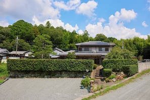 A traditional Japanese house with a tiled roof, surrounded by lush greenery and a stone wall.