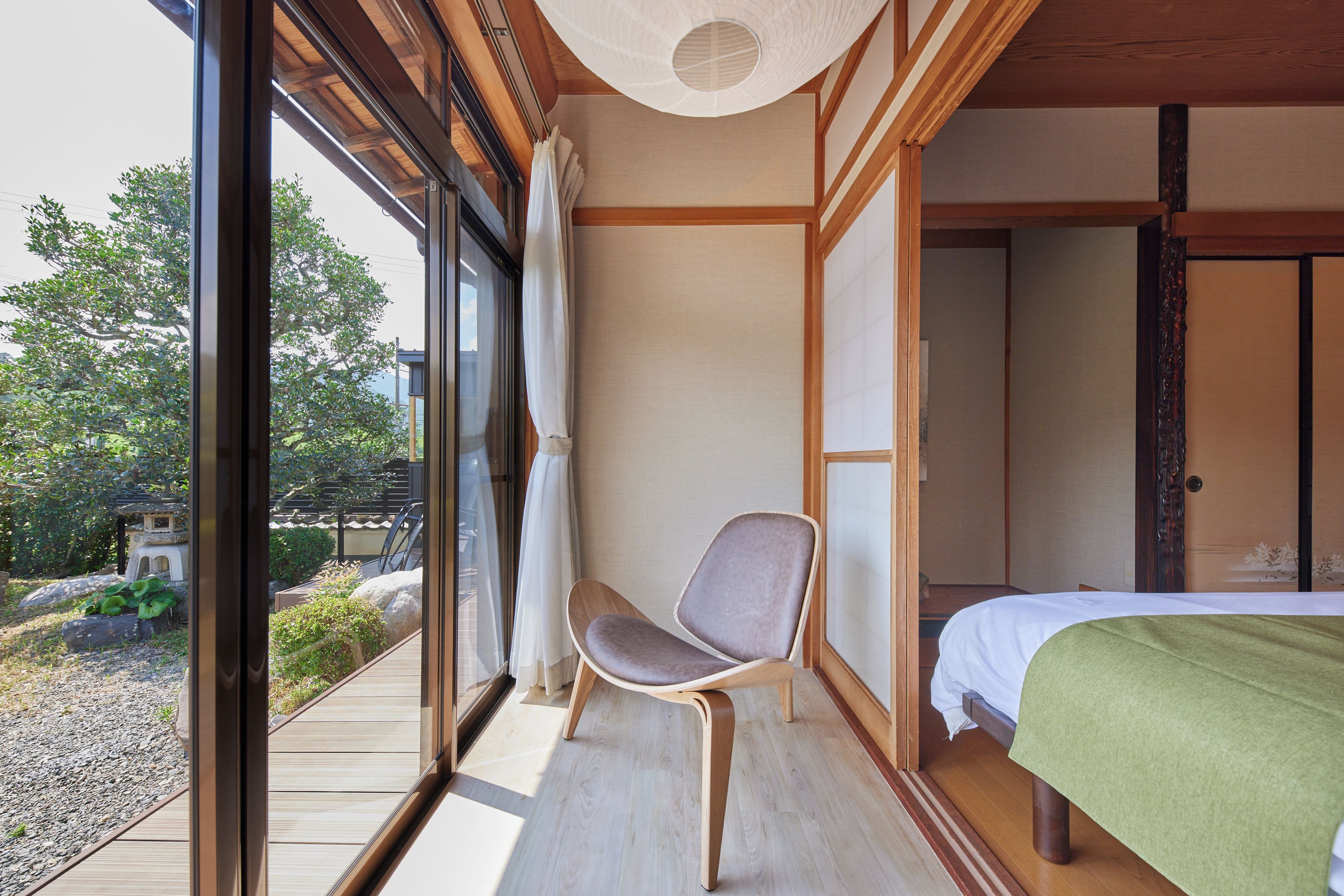 A room with a bed, a chair, and a view of a garden through a large window.
