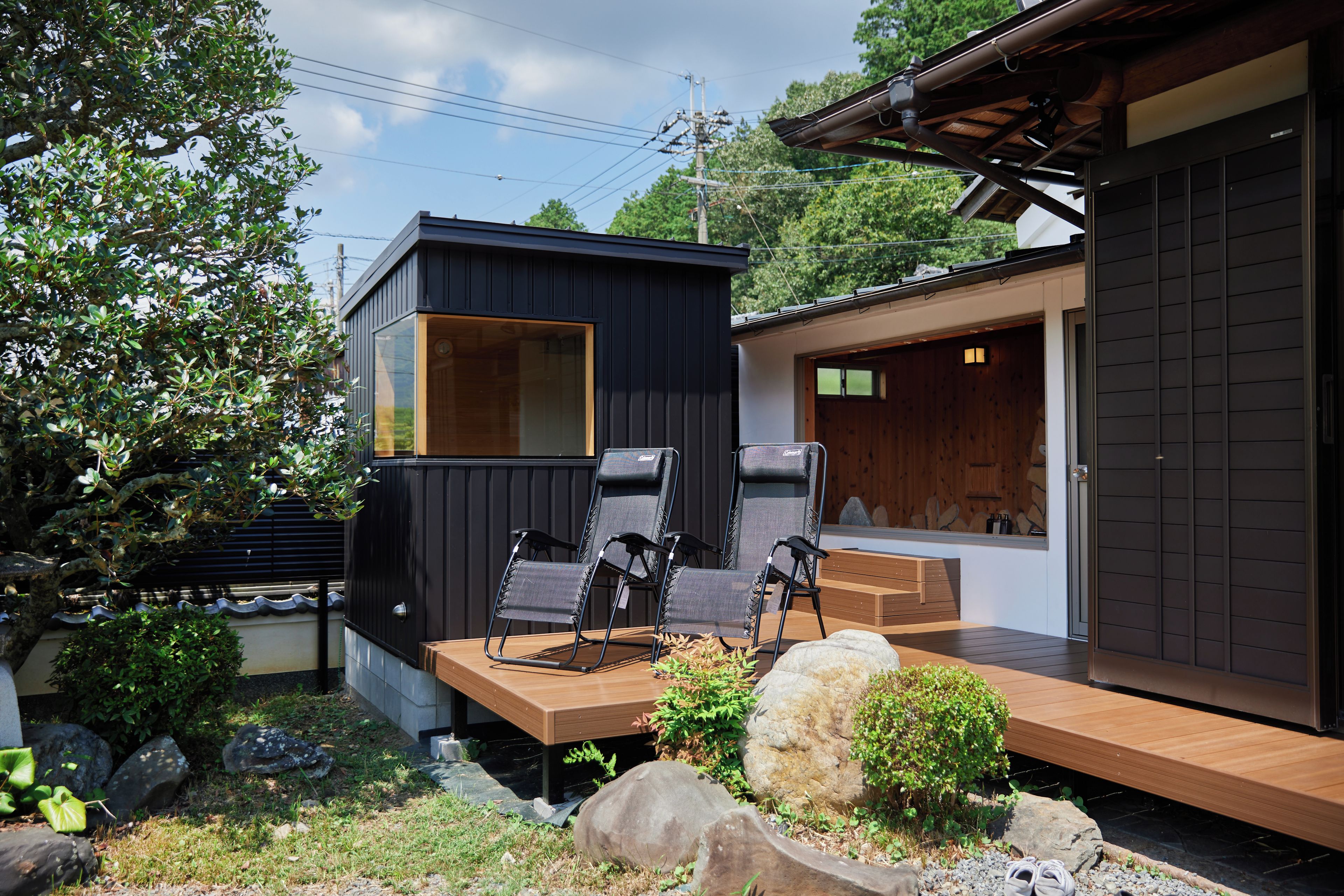 Un espacio moderno para sentarse al aire libre con terraza de madera, dos sillas plegables y una mesita.