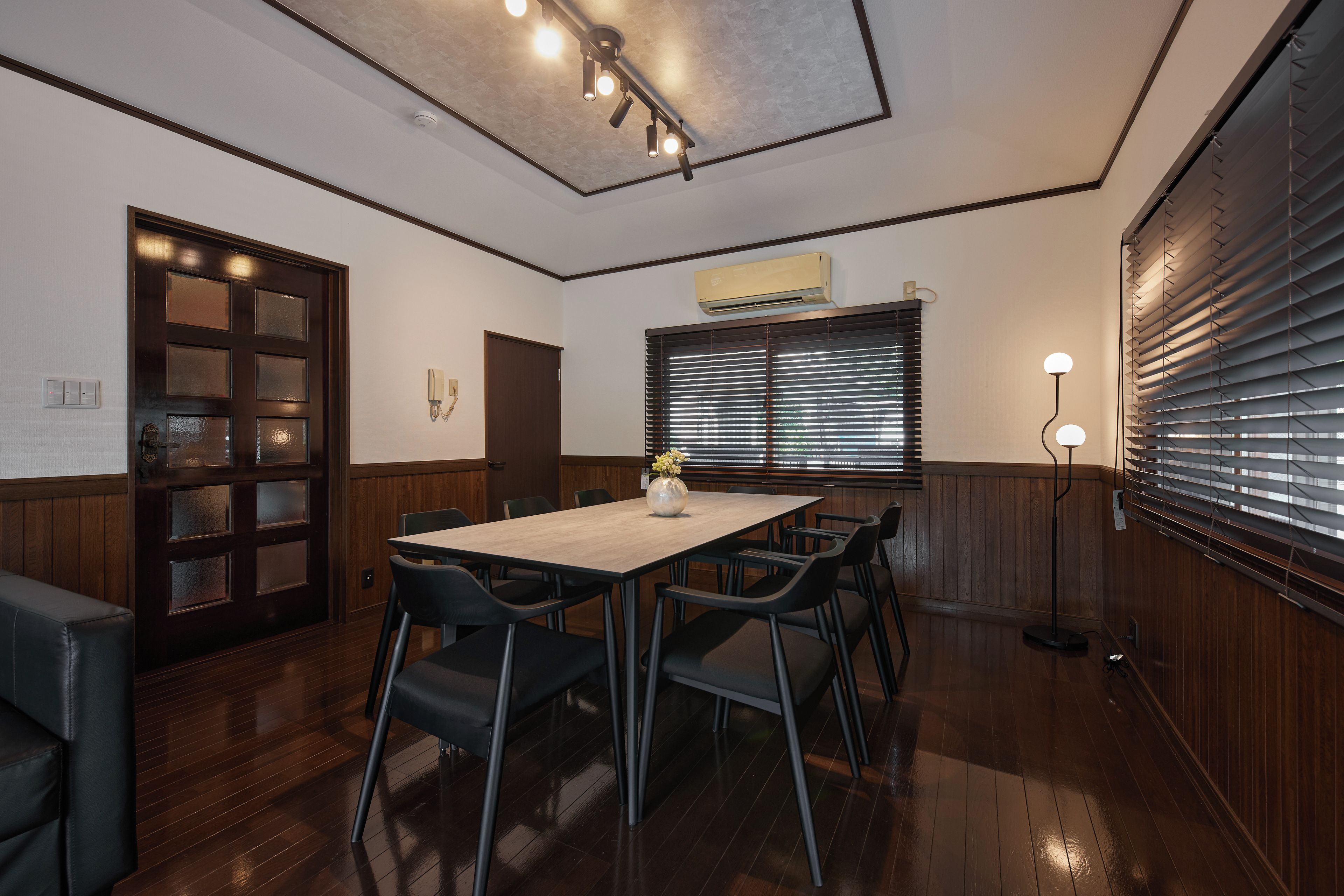 A conference room with a wooden table, chairs, a vase with flowers, a phone, and a wall-mounted air conditioner.