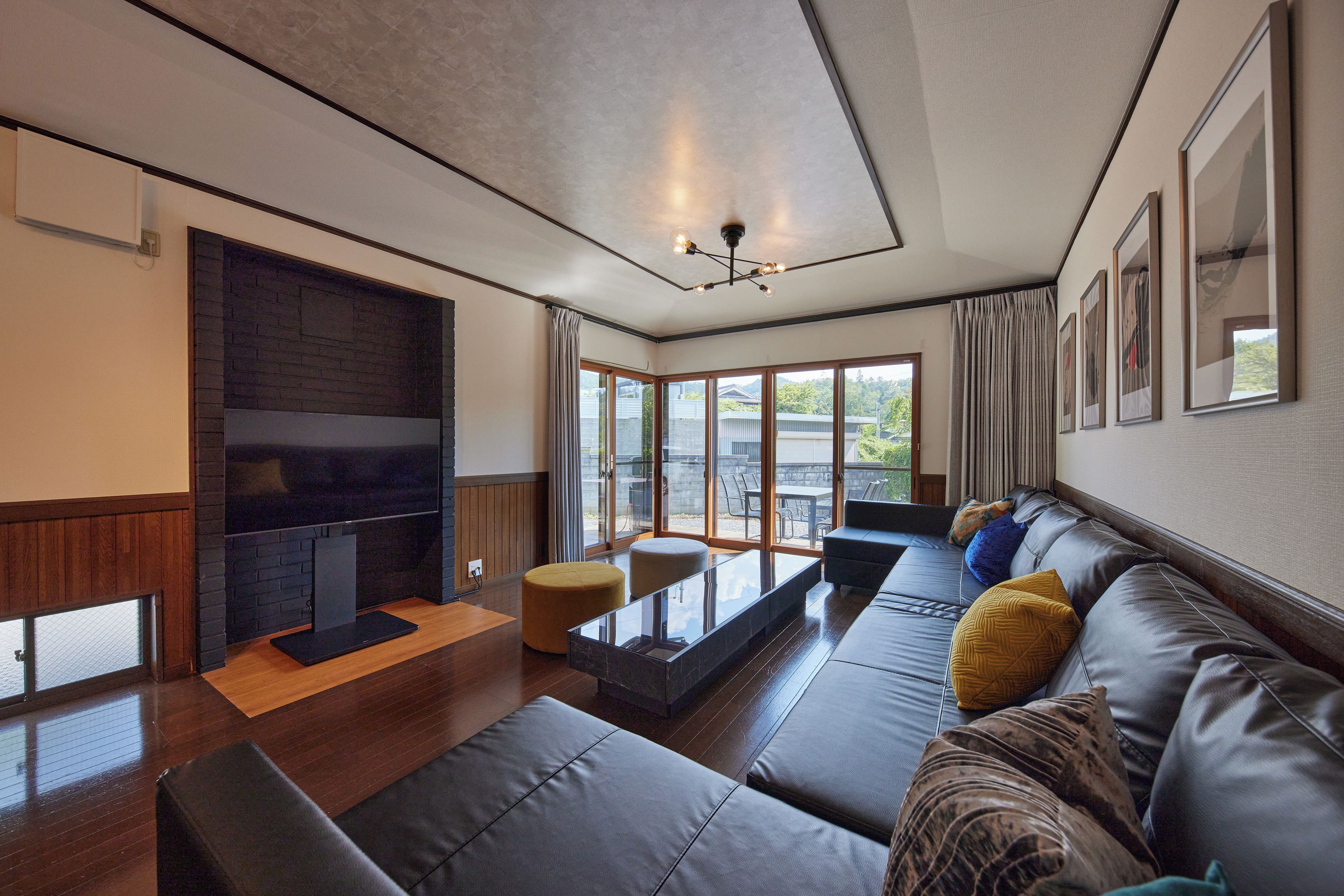 A modern living room with a fireplace, leather sofa, and large windows.