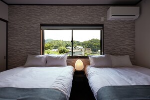 Habitación de hotel con dos camas, una ventana con vistas a edificios y zonas verdes, y un equipo de aire acondicionado en la pared.