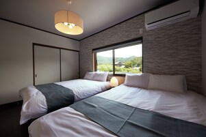 Un dormitorio con dos camas, una ventana con vistas a la vegetación y un equipo de aire acondicionado en la pared.
