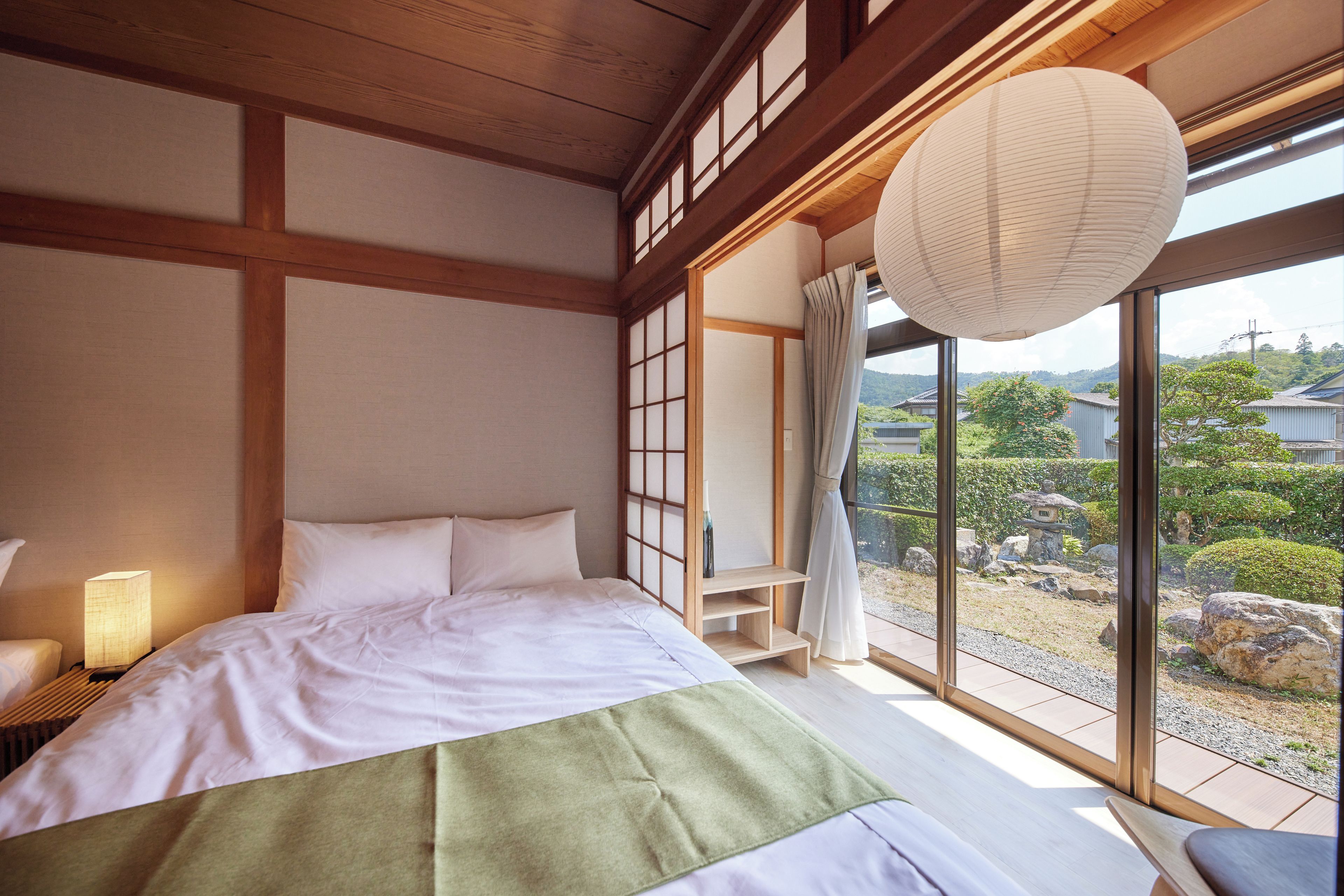 A traditional Japanese-style bedroom with a large window, wooden beams, and a bed with white bedding.