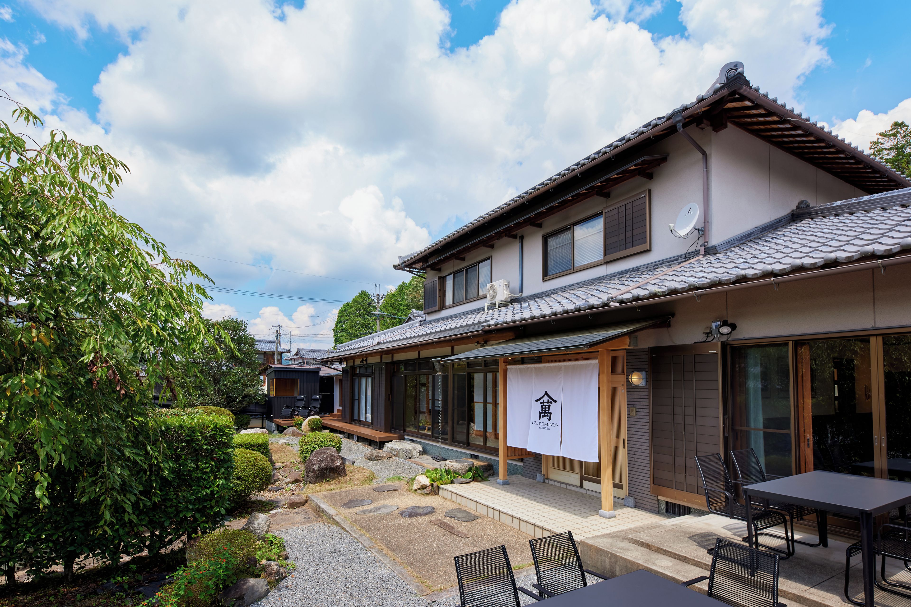 A traditional Japanese building with a tiled roof, a small garden with rocks and shrubs, and outdoor seating.